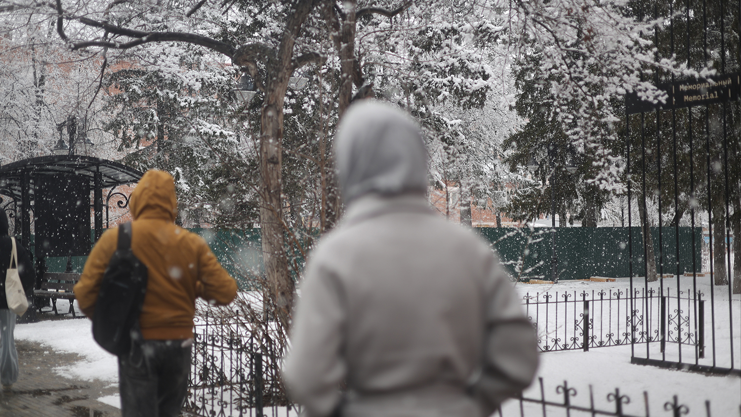 Pedestrians walk past the former memorial site along Lenin Avenue, with the city administration to their left and the NKVD museum to their right.